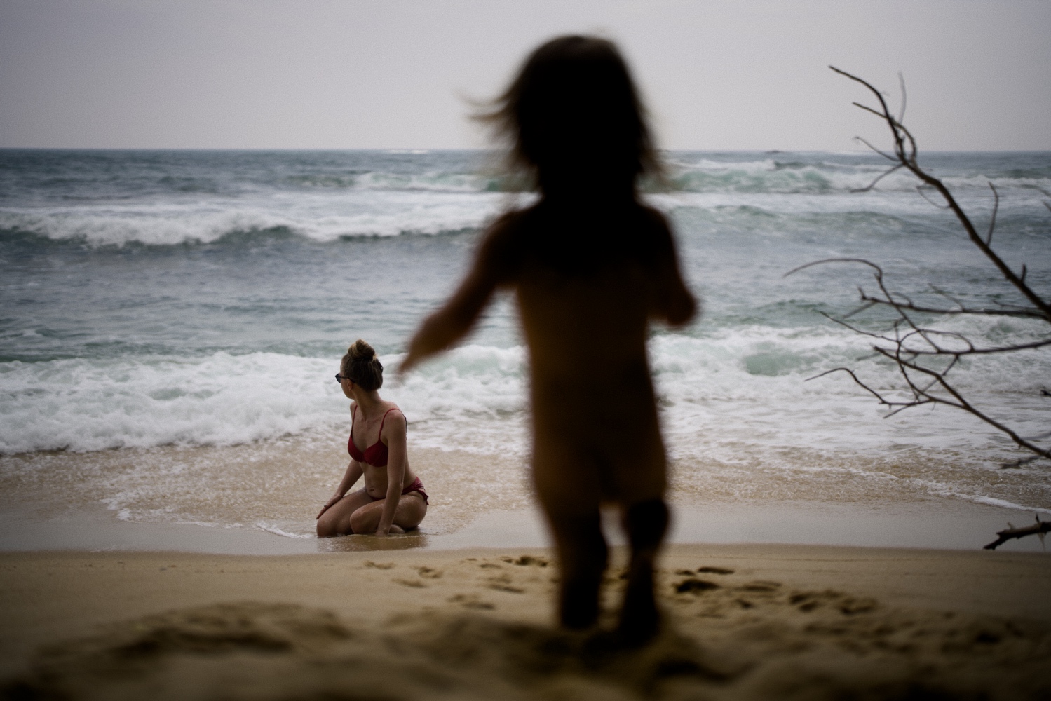 My daughter running downhill to meet her mother down the hill. Mother is playing with waves in the beautiful beach.