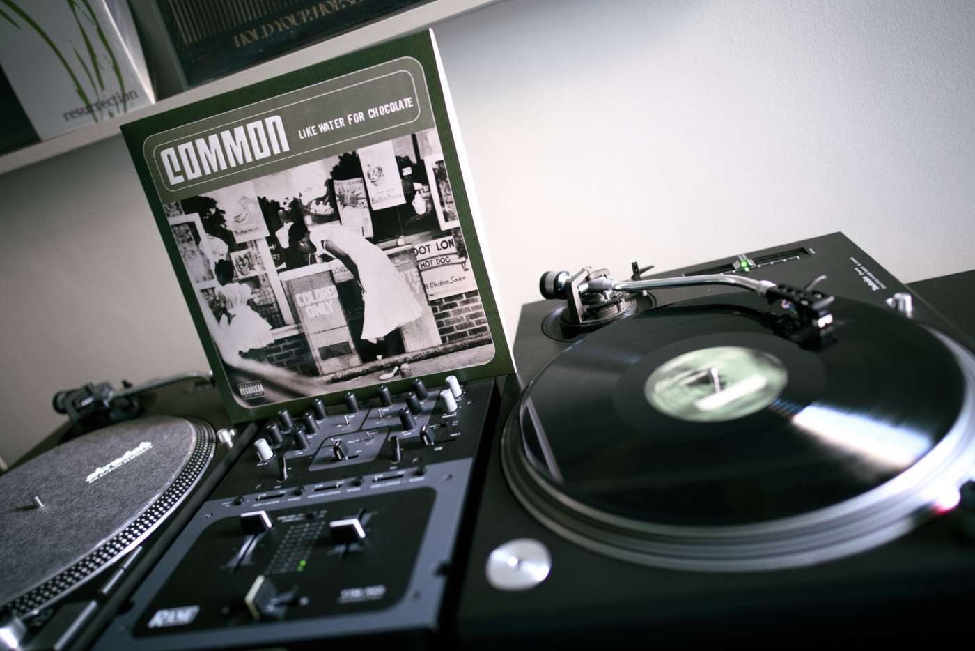 Cover of a vinyl record &ldquo;Like Water for Chocolate&rdquo; by Common, put betweet two turntables. The record is spinning on the right turntable.
